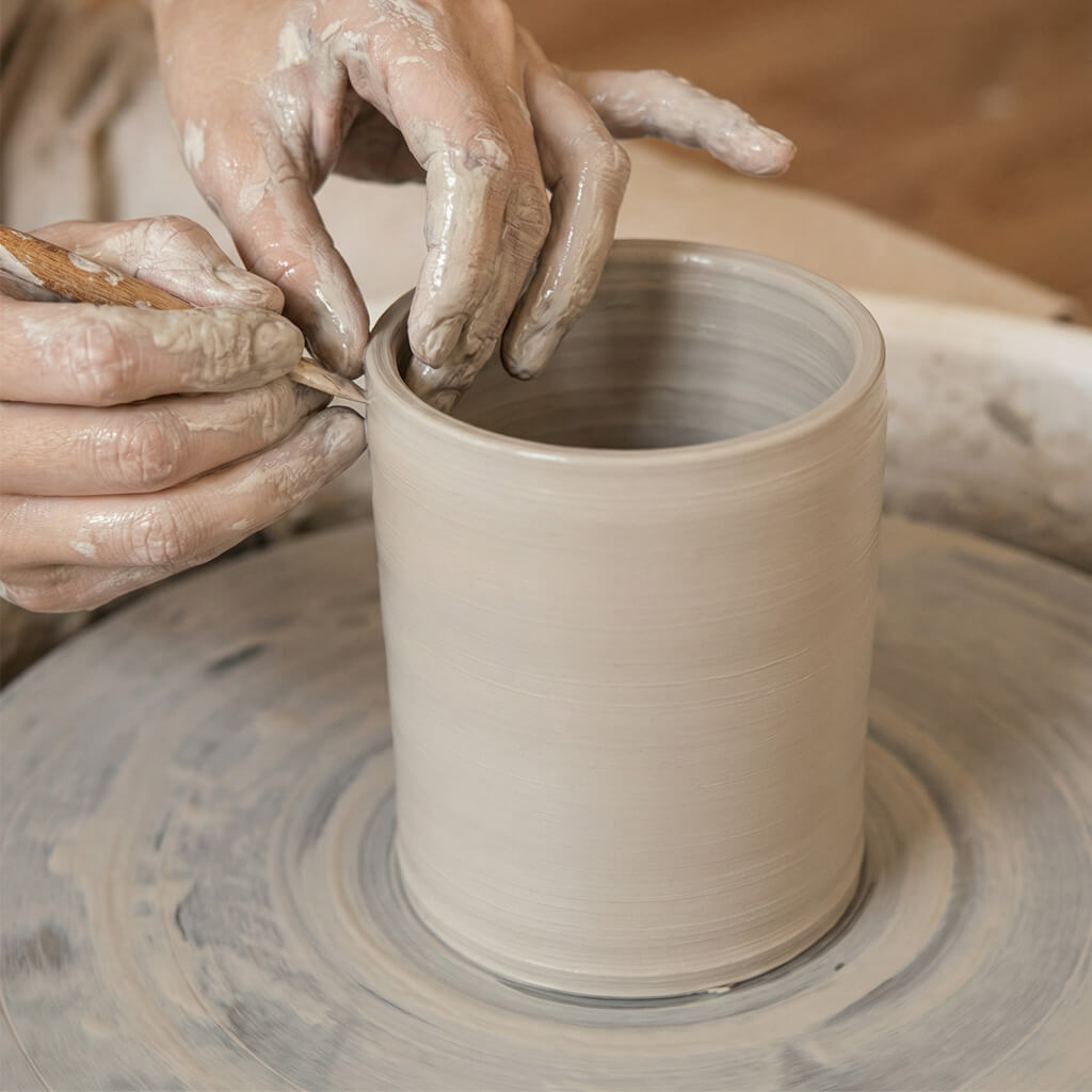 A Hollow Paw artist's hand refining the thrown clay urn body, meticulously shaping the foundation for a handcrafted pet memorial.